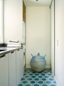 Kugelförmiger Korb mit Deckel auf gemustertem Fliesenboden im Waschraum