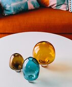 Retro-Vasen aus braunem und blauem Rauchglas auf weißem Coffeetable vor orangefarbenem Sofa