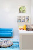 Hellblaues Lackleder-Sofa, davor blau-weiß gestreifter Teppich mit Bodenkissen neben Kinderbett