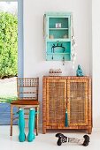 Vintage wall cupboards and rattan sideboards next to bamboo chairs and turquoise rubber boots in a summery atmosphere