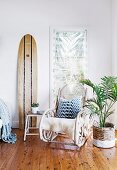 Exotische Sitzecke mit Schaukelstuhl, Surfbrett und Palme in einem Korb mit Colour-Dipping