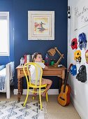 Boy sitting at desk in bedroom with super-hero masks hung on wall