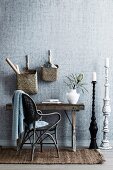 Dark rattan chair in front of rustic wooden console table, baskets on wall, floor candle holder on the side