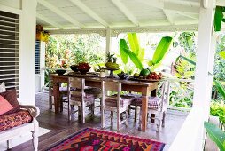 Dining table with simple wooden chairs and fruit bowls on a wooden terrace in a tropical setting