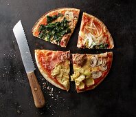A pizza with spinach, mushrooms, artichokes, Parma ham, onions and tuna fish, sliced