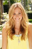 A blonde woman wearing a light yellow top and a fashionable necklace