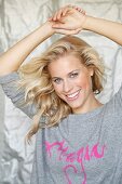 A blonde woman holding her arms above her head wearing a grey jumper with the word 'Magic' written in pink