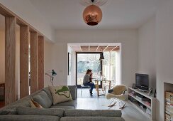 Corner sofa and classic rocking chair with fur blanket; woman and child in conservatory extension with dining area and view of garden