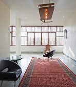 Retro Ledersessel auf Orientteppich in puristischem Wohnraum; gedämpftes Licht durch Fensterfront mit Sonnenschutz