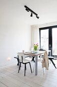 Dining area below black spotlights on lighting rail in minimalist interior with white-painted wooden floor