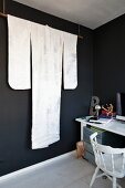 Elegant white kimono displayed on rod suspended from ceiling in black-painted room next to desk