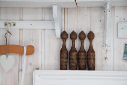 Old wooden skittles on narrow shelf against wooden wall stained white