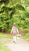Little girl carrying basket of lily-of-the-valley along woodland path