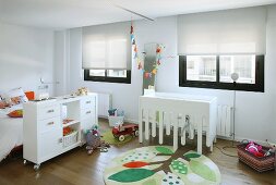weiße Möbel und farbige Elemente wie ein runder Teppich mit stilisiertem Baummotiv in modernem Kinderzimmer