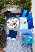 Sommerlicher Balkon mit gedecktem Tisch von oben gesehen; Kissen in Aquatönen auf weissen Outdoor-Möbeln