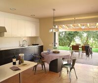 Retro metal chairs at round table in open-plan kitchen adjoining terrace with view into garden