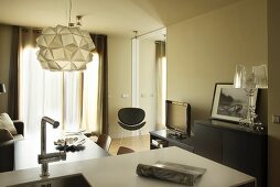 Blick über Küchentheke in Wohnraum, Designer-Hängeleuchte über Essplatz, im Hintergrund schwarzer Stuhl mit Retro Flair
