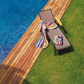 Lawn and wooden deck edging pool; brightly striped towels on modern sun lounger