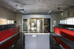 Island counter between kitchen counters with red fronts; stainless steel fridge in background