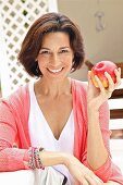 Dark-haired woman wearing top and cardigan holding apple