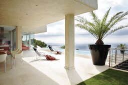 Designer Essplatz unter auskragendem Betondach und Sonnenliegen auf der Pool-Terrasse eines modernen Ferienhauses am Meer