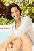 A brunette woman by a pool wearing a light grey top and cardigan