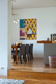 Grey-covered chairs around table below Art-Deco pendant lamp in dining room with modern artwork on wall