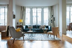 Couch with black and white patterned cover and fifties-style armchair opposite modern sofa below window in lounge area