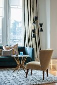 Retro armchair and side table in front of couch below window next to fifties-style standard lamp