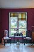 Two chairs and table in front of window with Roman blinds in purple wall