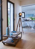 Low sideboard on castors, industrial-style tripod lamp and view into kitchen-dining room
