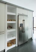 Stainless steel, side-by-side fridge freezer flanked by tall cabinets and open-fronted shelving