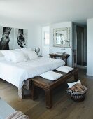 Rustic wooden bench at foot of double bed in bedroom with large photos on wall