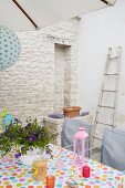 Tealight holders and candle lanterns on spotted tablecloth on terrace with stone façade of house in background