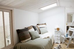 Striped cushions on bed below skylight in simple room