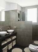 Doppelwaschtisch aus Holz mit Aufsatzschüsseln, dahinter geflieste Trennwand zur begehbaren Dusche