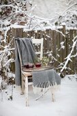 Tray of mulled wine and blanket on old wooden chair in snowy garden
