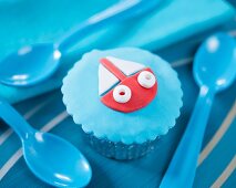 A cupcake decorated with a fondant boat on a blue background