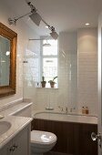 Modernes weiß gefliestes Bad mit traditionellem Flair, Badewanne hinter Glasscheibe mit Regendusche, Tolomeo Wandleuchten vor Spiegel im Goldrahmen