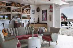 Fifties-style sofa set in rustic room with white wood panelling; open sliding door with view of jetty and boat