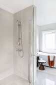 Floor-level shower with glass door, side table in background next to bathtub below window in modern bathroom with vintage ambiance