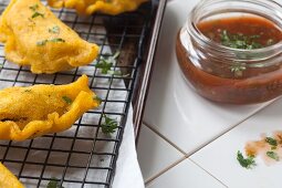 Colombian empanadas on a cooling rack with salsa