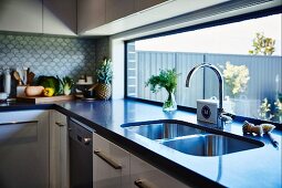 Twin sink in dark counter below long ribbon window in modern fitted kitchen