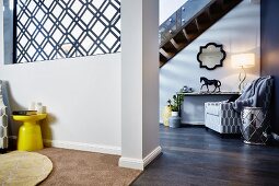 Partition wall with grille element, yellow side table, seating area below staircase in background in open-plan interior