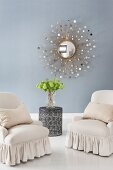 Elegant armchairs with valances on white-painted wooden floor and sunburst mirror on blue wall