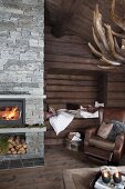 Gemütliche Wohnzimmerecke, brauner Ledersessel vor Alkoven in Holzbohlenwand, seitlich Kaminfeuer