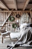 Bedroom in rustic wooden house with cane chair next to bed with linen bedspread and headboard made from reclaimed boards