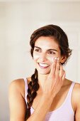 Young, brunette woman with braided hair applying cream to face