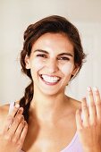 Young, brunette woman with braided hair applying cream to face