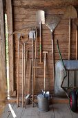 Gardening tools hung up in garden shed next to zinc watering can and wheelbarrow